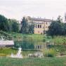 A swimming pool in a large garden with a yellow building in the background.