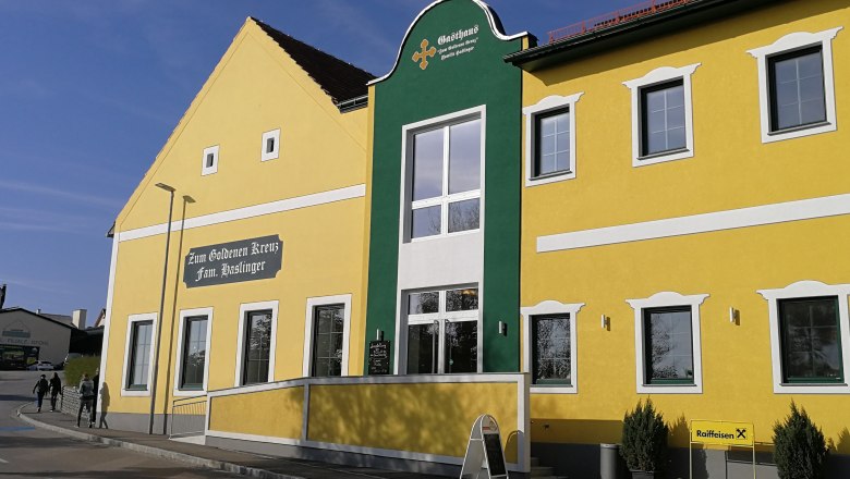 Gelbes Gebäude mit grüner Fassade und der Aufschrift 'Zum Goldenen Kreuz Fam. Haslinger'.