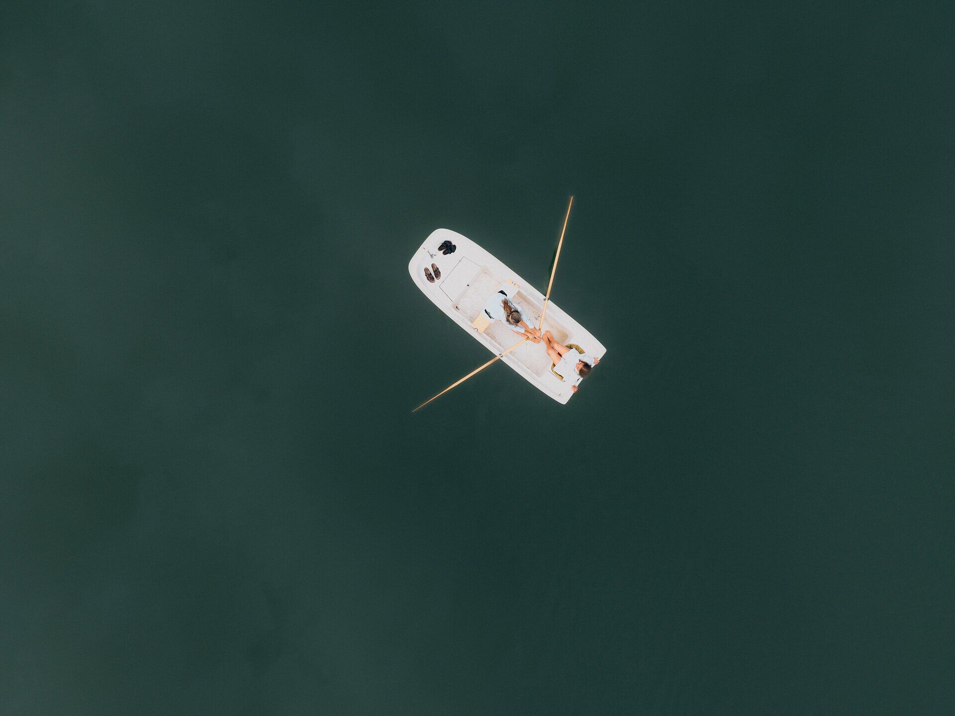 Drohnenaufnahme eines weißen Ruderboots mit zwei Personen auf dem ruhigen, dunkelgrünen Wasser des Stausees Ottenstein im Waldviertel.