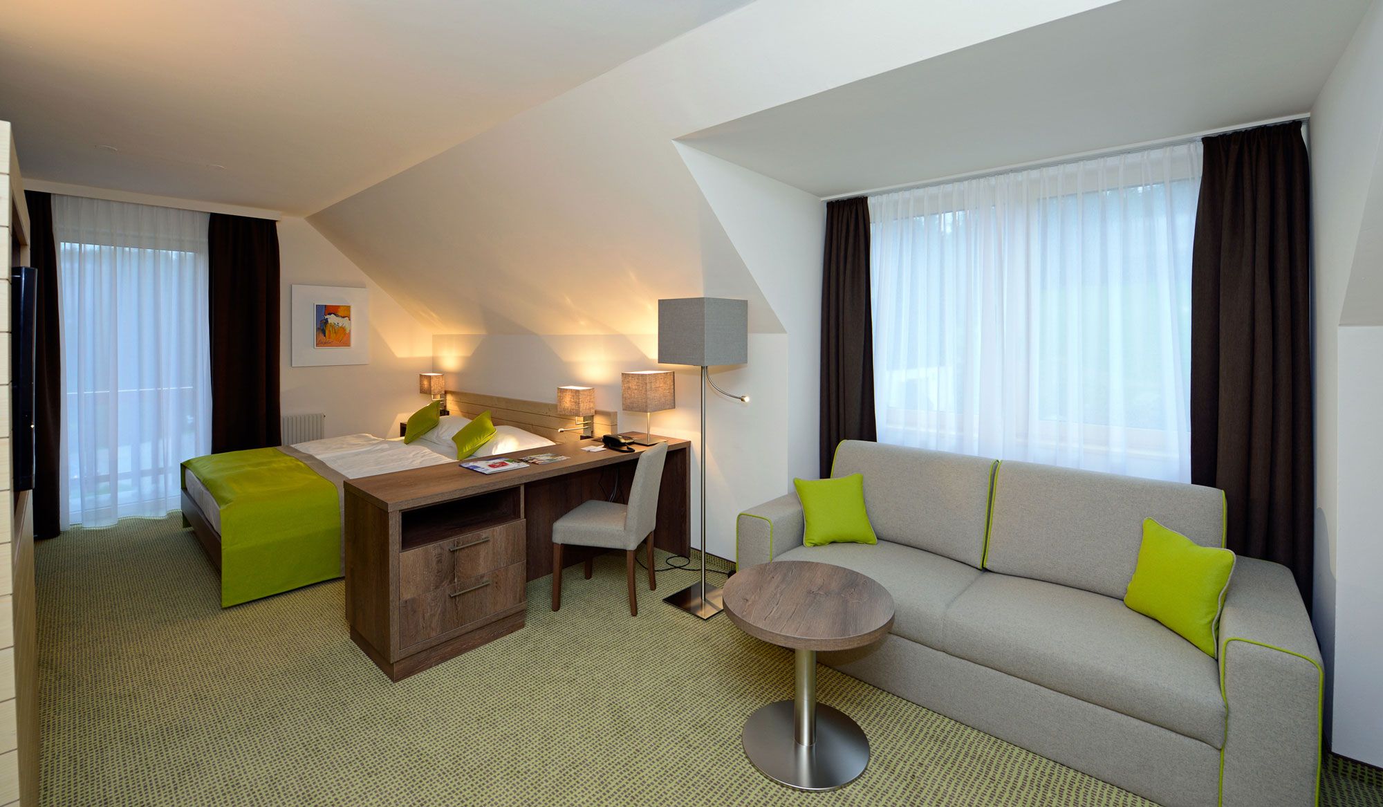Hotelzimmer mit Bett, Schreibtisch, Sofa und Tisch, modern eingerichtet.