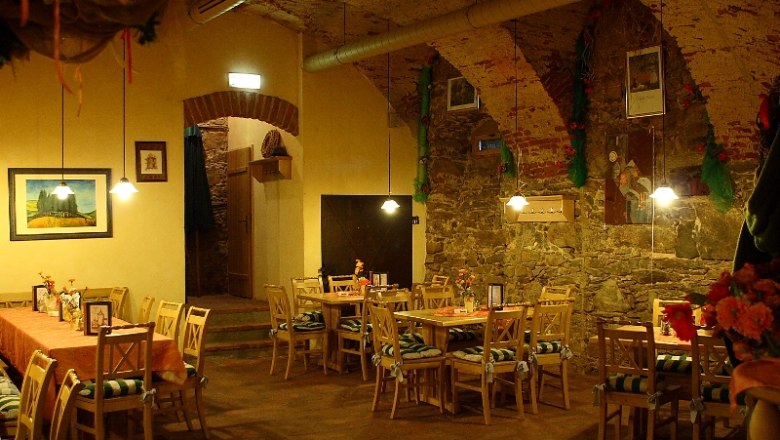 Gemütlicher Gastraum mit Holztischen und Stühlen, dekoriert mit Blumen und Bildern an den Wänden.