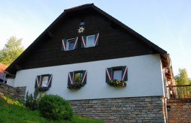 Ein traditionelles Haus mit Holzverkleidung und bunten Fensterläden, umgeben von grüner Vegetation.