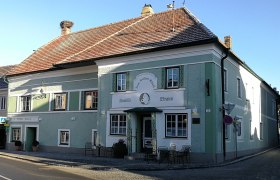 Ein traditionelles Gasthaus mit grüner Fassade und dem Namen 'Zum weißen Rössl'. Vor dem Gebäude stehen Tische und Stühle.