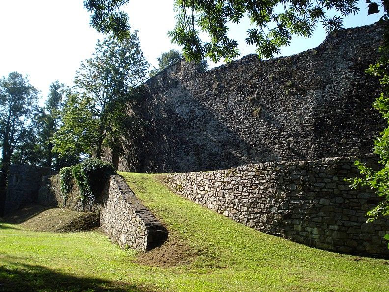 Alte Stadtmauer mit Grünfläche und Bäumen im Sonnenlicht.