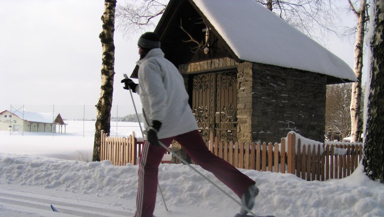 Person cross-country skiing in front of a snow-covered chapel.
