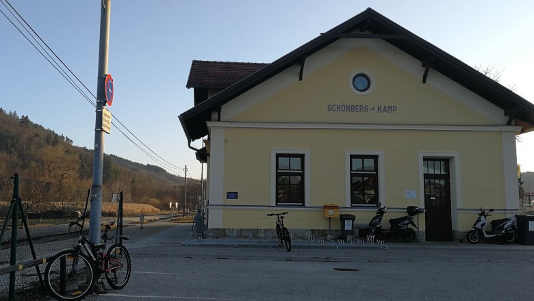 Bahnhof Schönberg am Kamp mit Fahrrädern und Rollern davor, umgeben von ländlicher Landschaft.