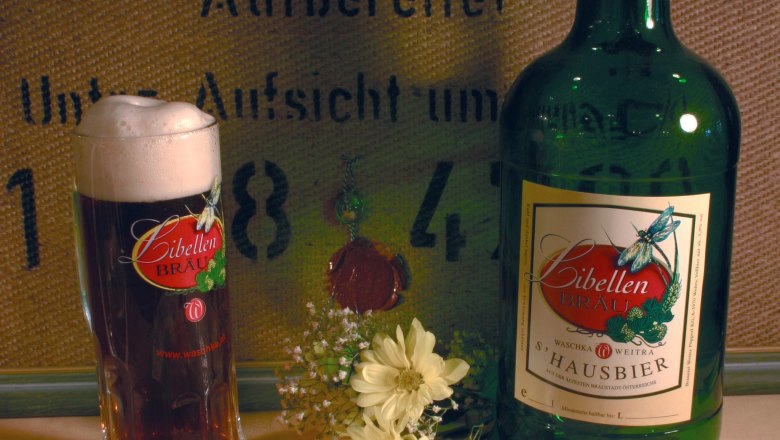 A glass and a bottle of Libellen Bräu beer with flowers in the foreground.