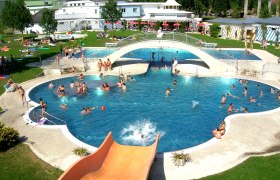 Freibad mit Pool, Br&uuml;cke und Rutsche, viele Menschen beim Schwimmen und Sonnenbaden.