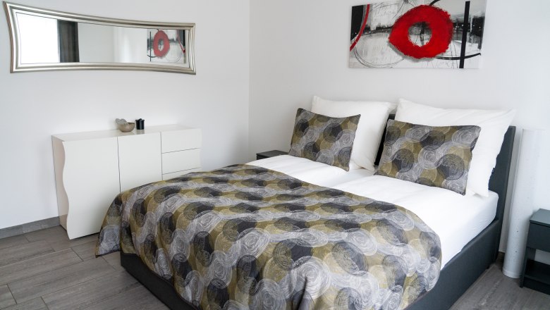 Modernes Schlafzimmer mit Doppelbett, abstraktem Kunstwerk und Spiegel.