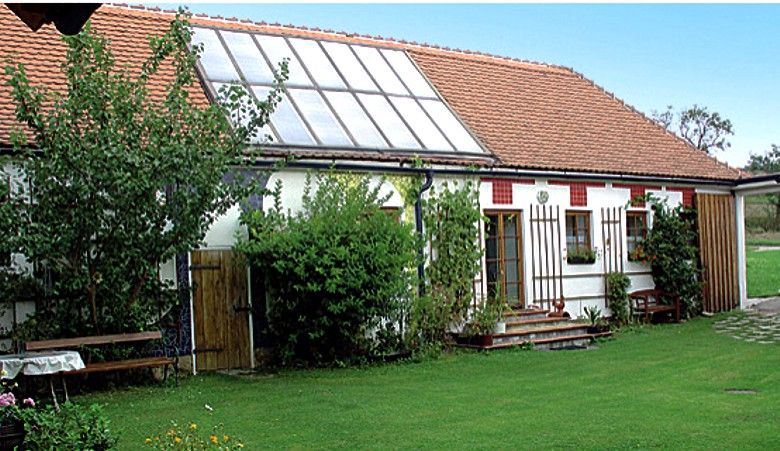 Ein traditionelles Gebäude mit Solarpanelen auf dem Dach und einem gepflegten Garten davor.