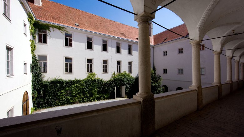 Innenhof eines historischen Gebäudes mit Arkadengang und Efeu bewachsenen Wänden.