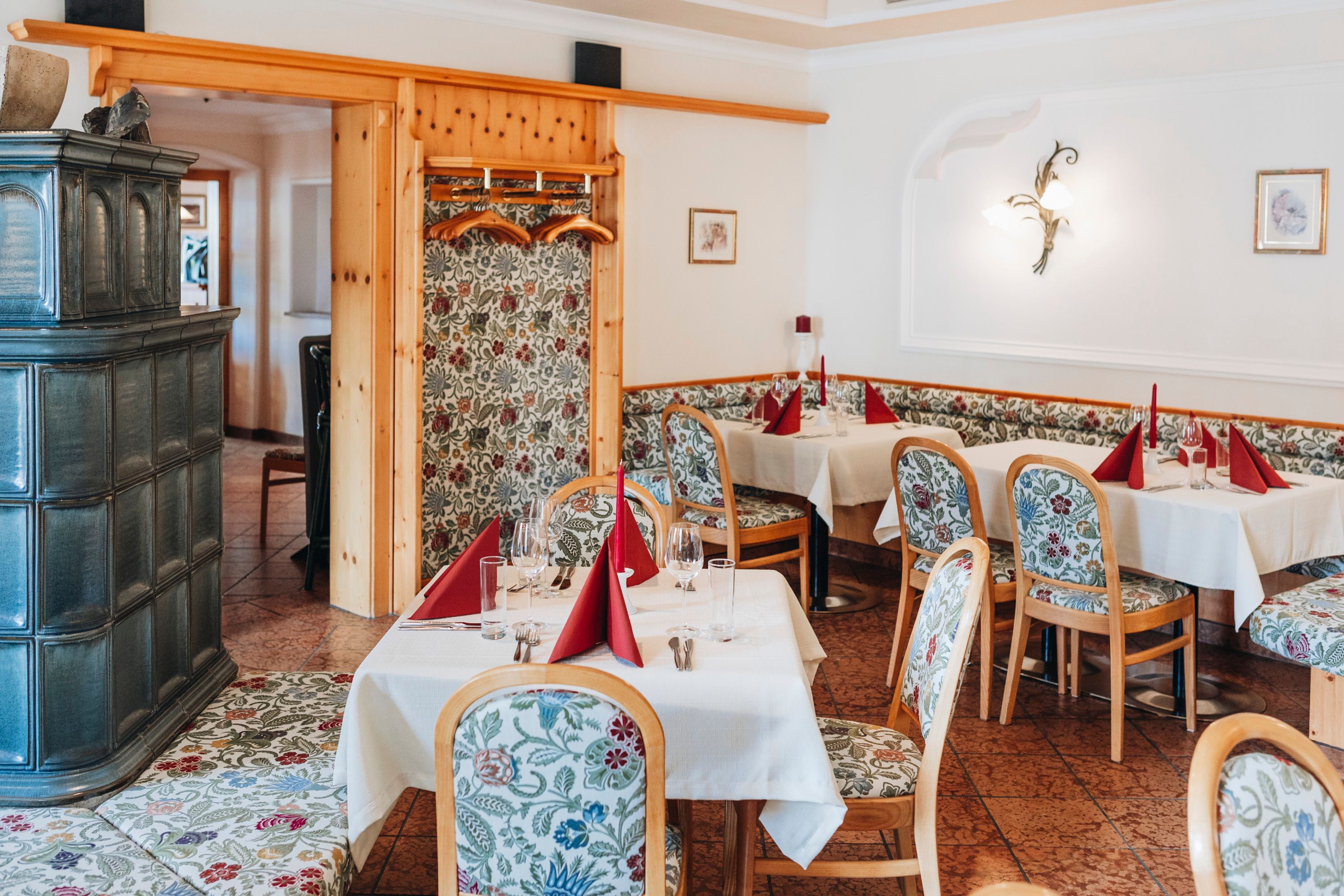 Gemütliche Wirtshausstube mit gedeckten Tischen und floral gemusterten Stühlen.