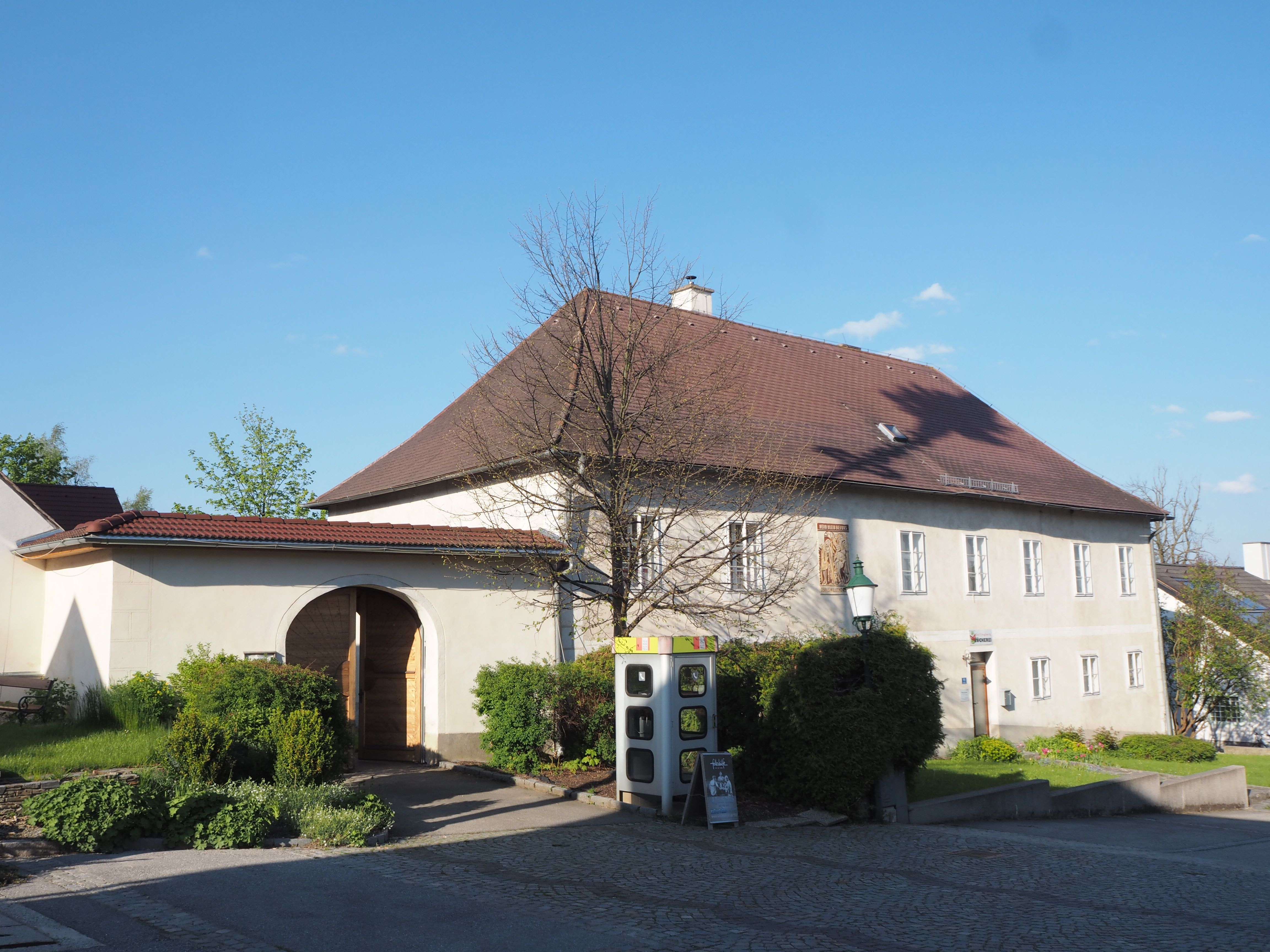 Historisches Gebäude mit Torbogen und Garten, blauer Himmel.