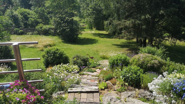 Ein gepflegter Garten mit Blumen, Büschen und einem Rasenbereich im Hintergrund.
