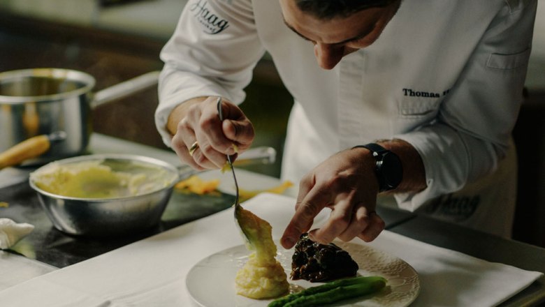 A chef prepares a dish of asparagus and mashed potatoes on a plate.