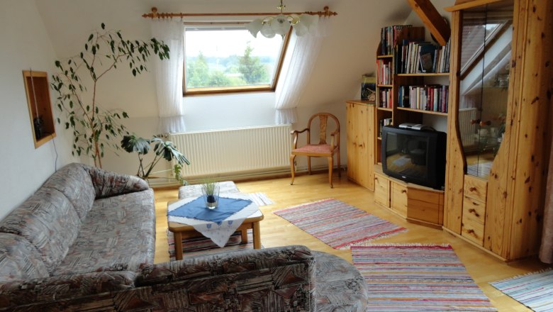 Gem&uuml;tliches Wohnzimmer mit Sofa, Holzm&ouml;beln und Fernseher.