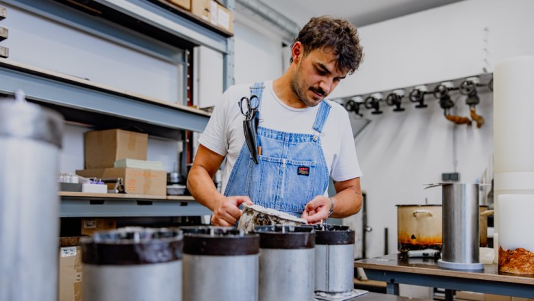 Mann in Werkstatt zieht Kerzen in Metallformen.