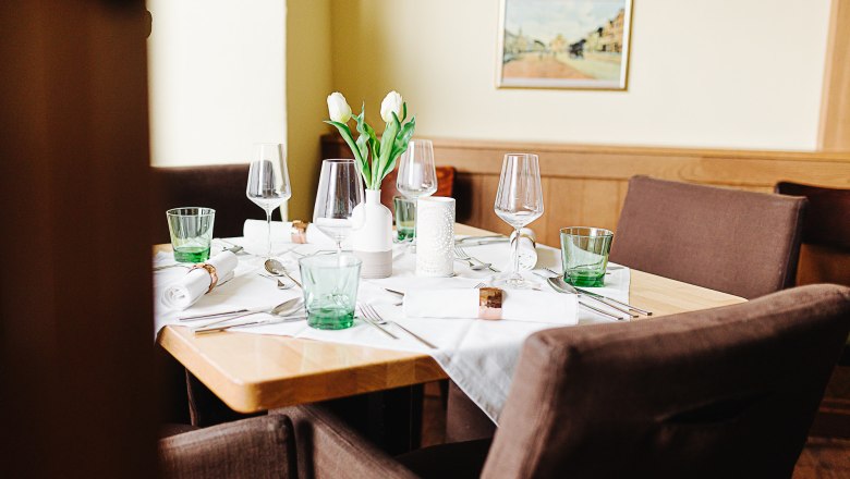 An elegantly laid table in an inn with glasses, cutlery and white tulips in a vase.