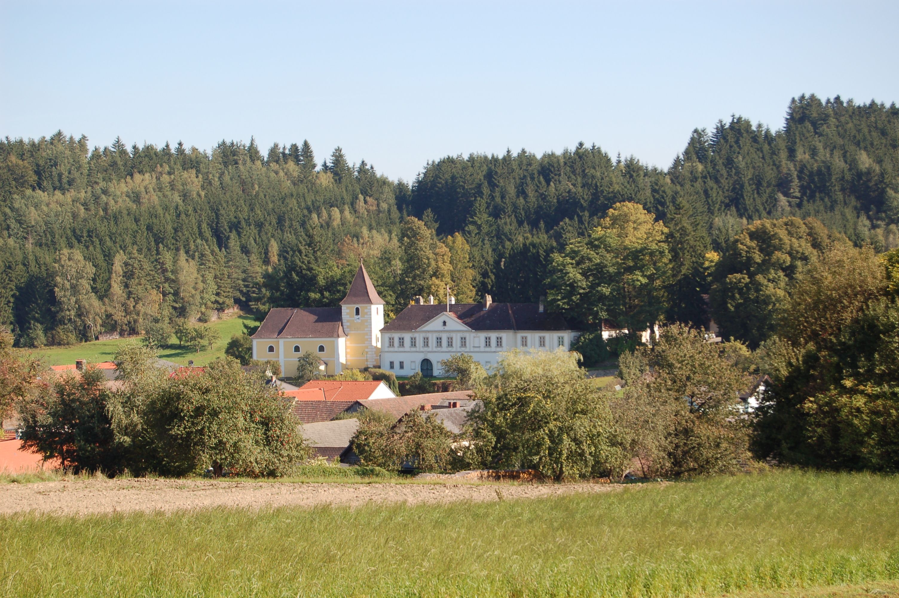 Ein Schloss mit gelbem Turm inmitten einer grünen Landschaft und umgeben von Bäumen.