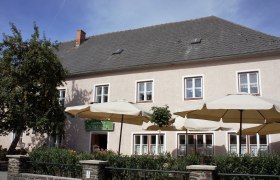Ein traditionelles Gasthaus mit Sonnenschirmen und einem Baum im Vordergrund.