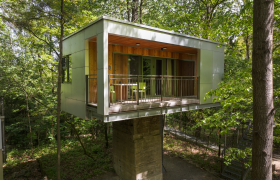 Modernes Baumhaus im Wald mit Balkon und Glasfront.