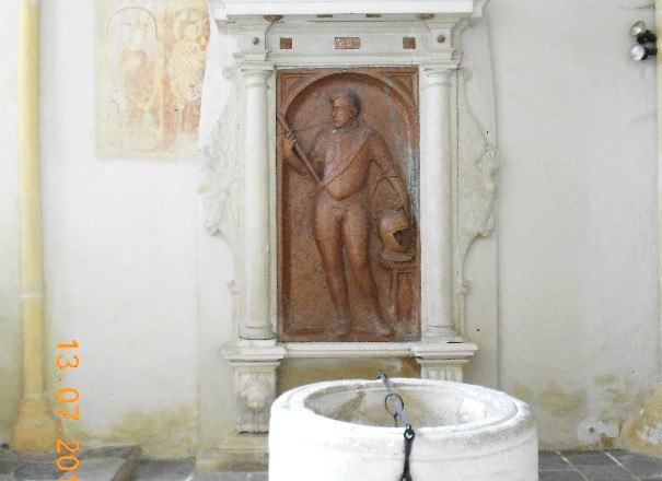 Grabmal mit Relief und Taufbecken in einer Kirche.
