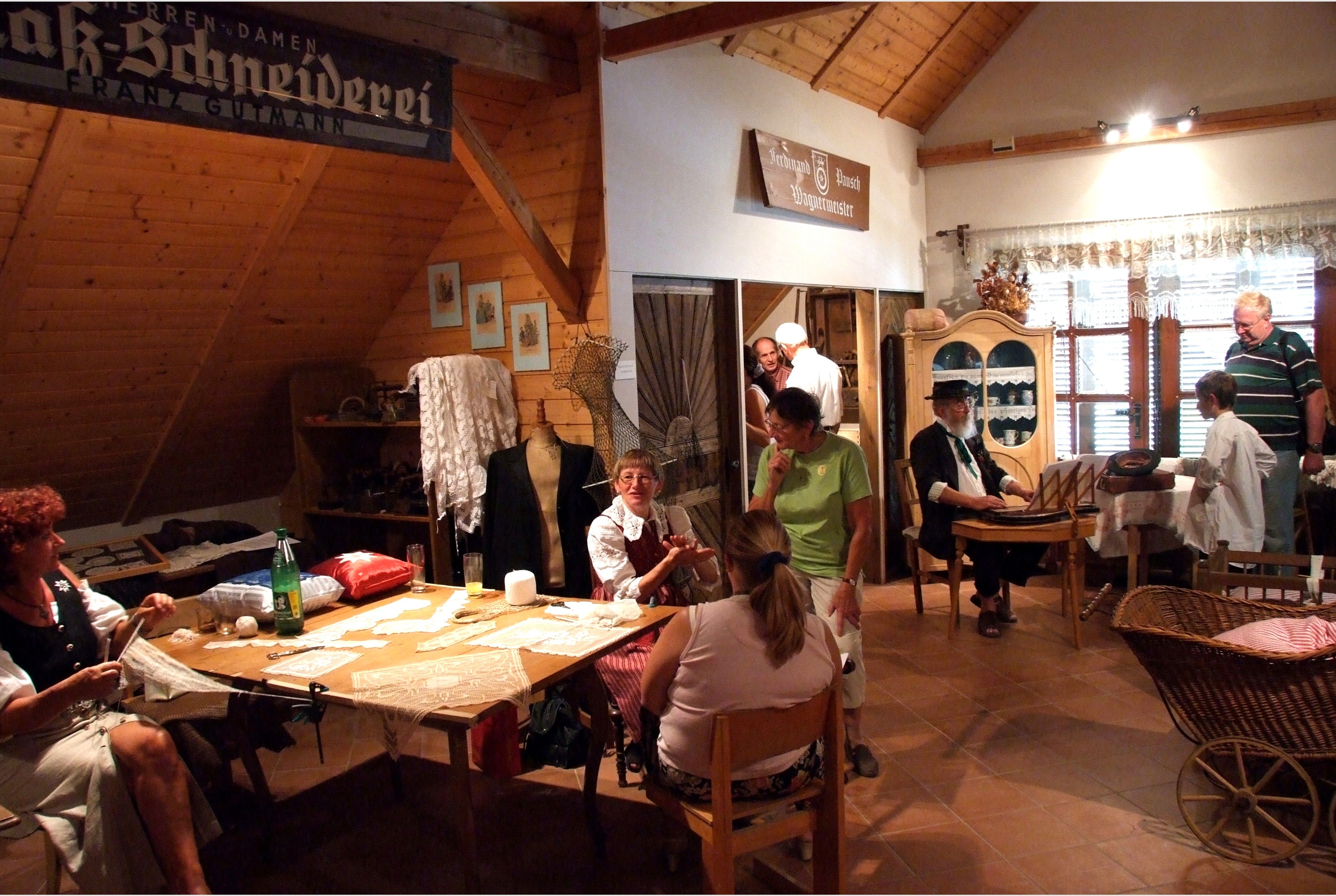 Innenansicht eines Heimatmuseums mit Menschen in traditioneller Kleidung, die handwerkliche Arbeiten zeigen.