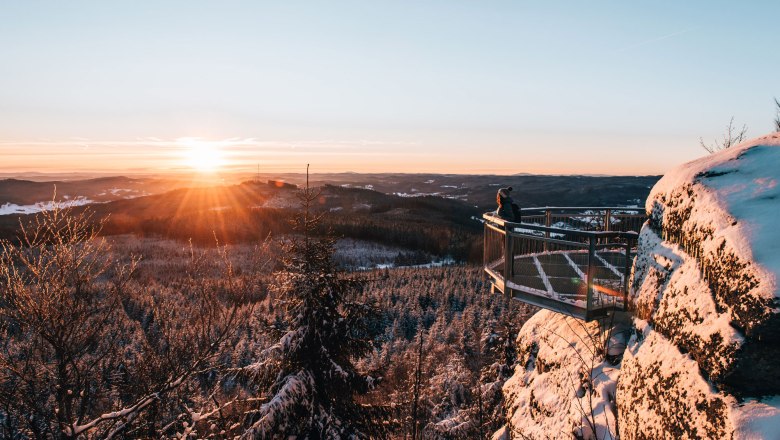 Person auf einer Aussichtsplattform im verschneiten Waldviertel bei Sonnenuntergang.