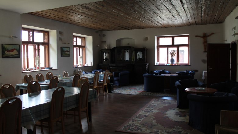 Ein gemütlicher Raum mit Holztischen, Stühlen und Sofas, dekoriert mit Teppichen und Bildern an den Wänden.