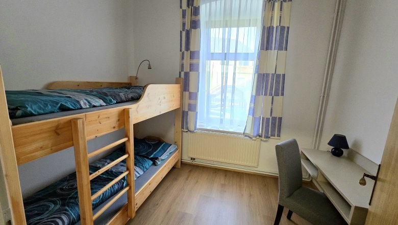 Kleines Schlafzimmer mit Etagenbett, Schreibtisch und Stuhl.