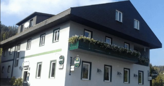 Ein zweistöckiges Gebäude mit einem Balkon voller Blumen und mehreren Gösser-Schildern an der Fassade.