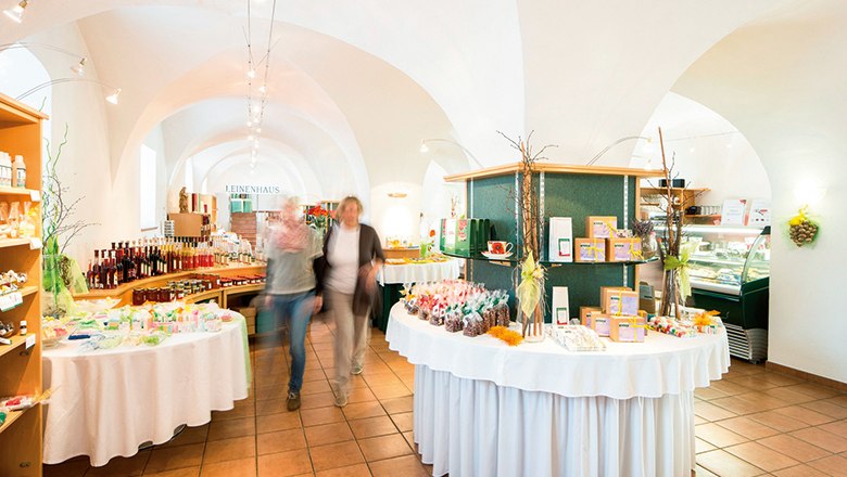 Innenansicht eines Ladens mit gewölbter Decke, Regalen voller Produkte und zwei unscharfen Personen.