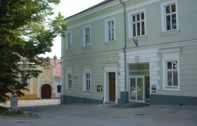 Ein zweistöckiges, hellgrünes Gebäude mit der Aufschrift 'Haus' über der Tür.