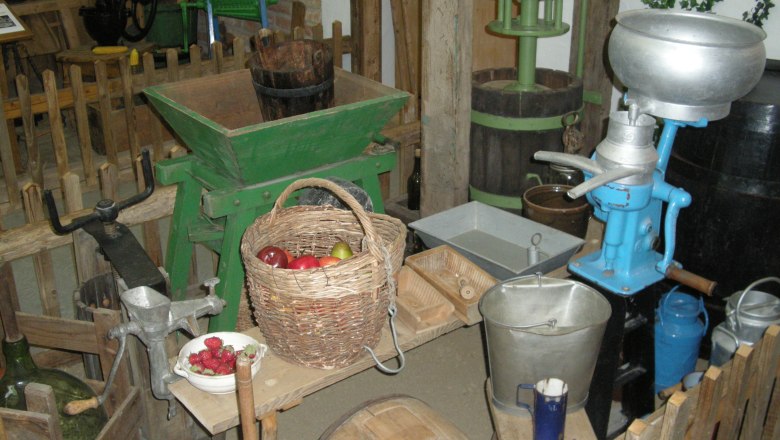 Alte landwirtschaftliche Geräte und ein Korb mit Obst in einem Museum.