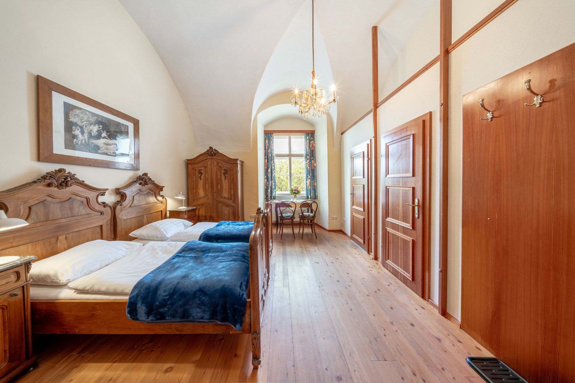 Ein elegantes Doppelzimmer mit antiken Holzmöbeln, einem Kronleuchter und einem Fenster mit Blick ins Grüne.