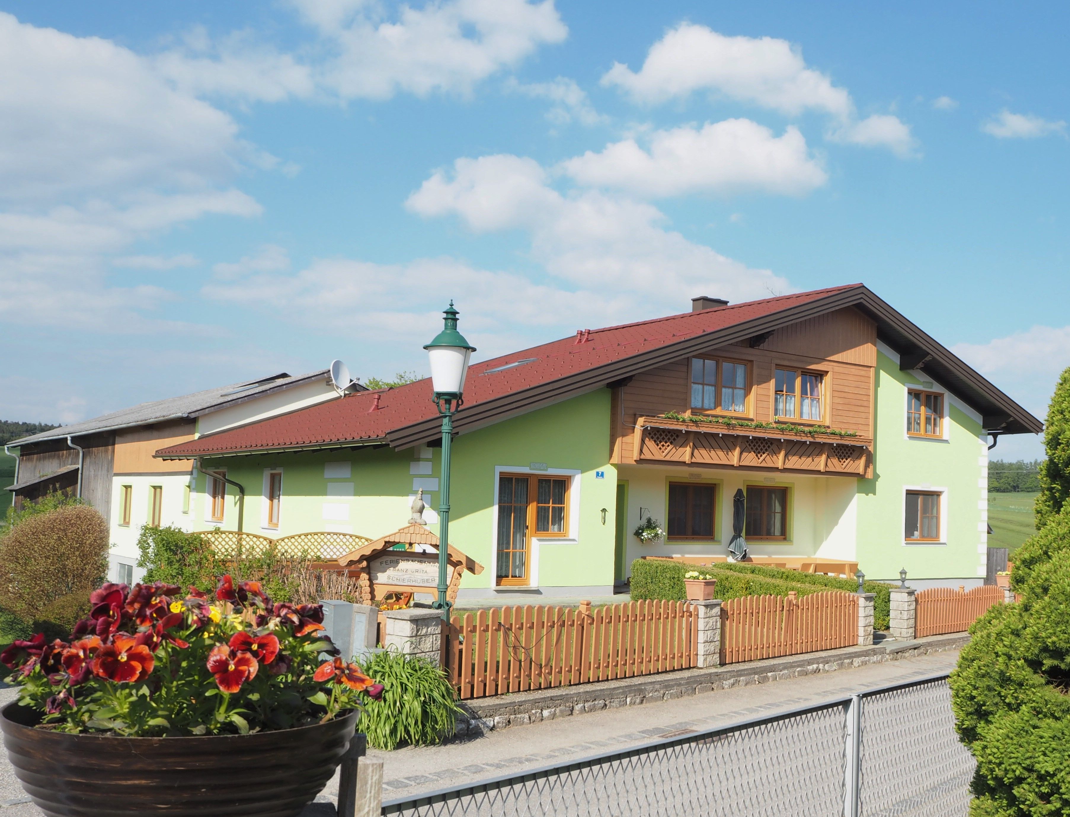 Ein Ferienbauernhof mit grünem Anstrich und Holzbalkon, umgeben von einem Holzzaun und Blumen im Vordergrund.