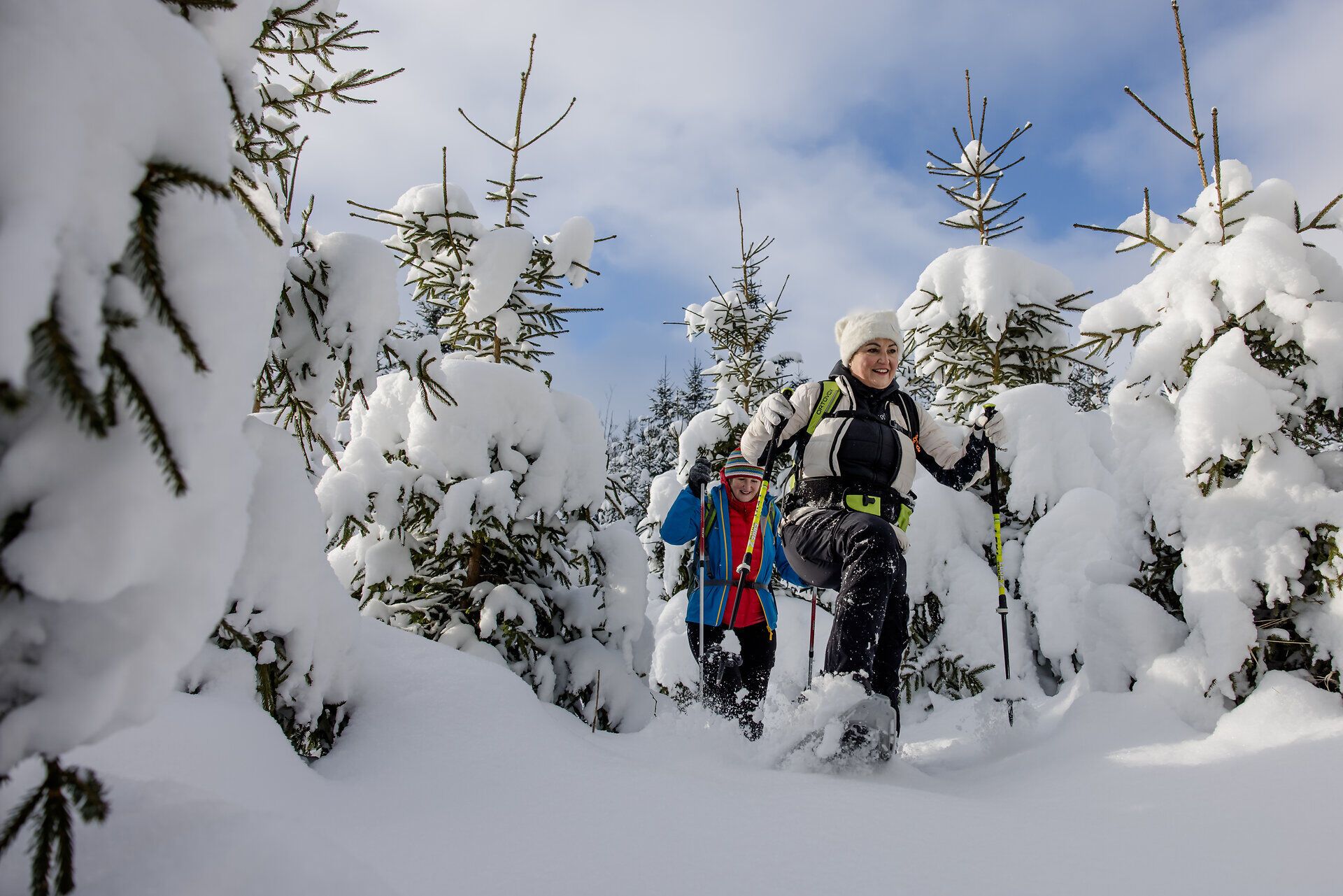 Zwei Personen beim Schneeschuhwandern durch verschneiten Wald.