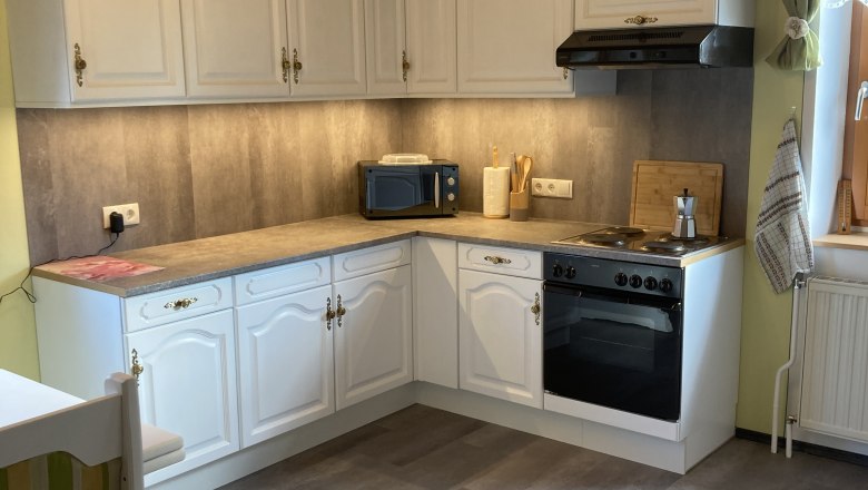 Geräumige Küche mit weißen Schränken, Herd, Mikrowelle und Holzdecke.