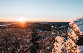 Person auf einer Aussichtsplattform im verschneiten Waldviertel bei Sonnenuntergang.
