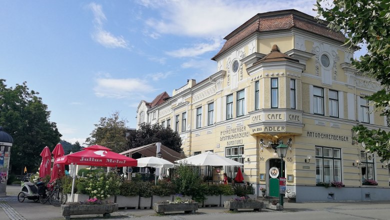 Historisches Gebäude mit Café und Terrasse, umgeben von Sonnenschirmen und Pflanzen.