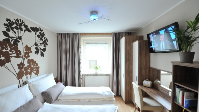 Ein modernes Schlafzimmer mit Doppelbett, Wanddekoration, Schreibtisch, Fernseher und Pflanzen.