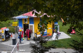 Kleines, buntes Infozentrum mit Spielzeug und Kleidung im Freien.