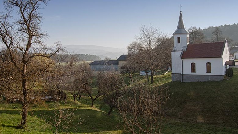 Landschaft mit Kirche und Bäumen bei klarem Himmel.