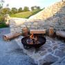 Barbecue area with fire pit and wooden benches in front of a stone wall.