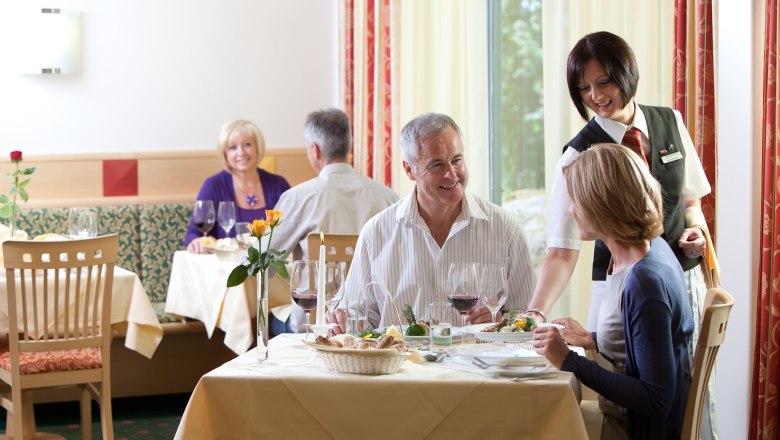 Ein Restaurant mit G&auml;sten, die an Tischen sitzen und von einer Kellnerin bedient werden.