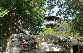Aussichtsturm der Gartenschule Langenlois umgeben von Bäumen und einer Steinmauer.