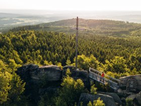 Aussichtsplattform auf einer Felsformation mit Blick &uuml;ber dicht bewaldete H&uuml;gel im Waldviertel, unter einem klaren blauen Himmel.