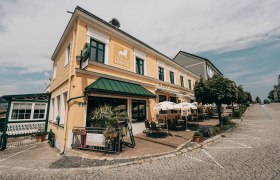Au&szlig;enansicht eines gelben Gasthauses mit Terrasse und Sonnenschirmen.