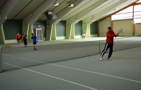 People play tennis in an indoor tennis hall.