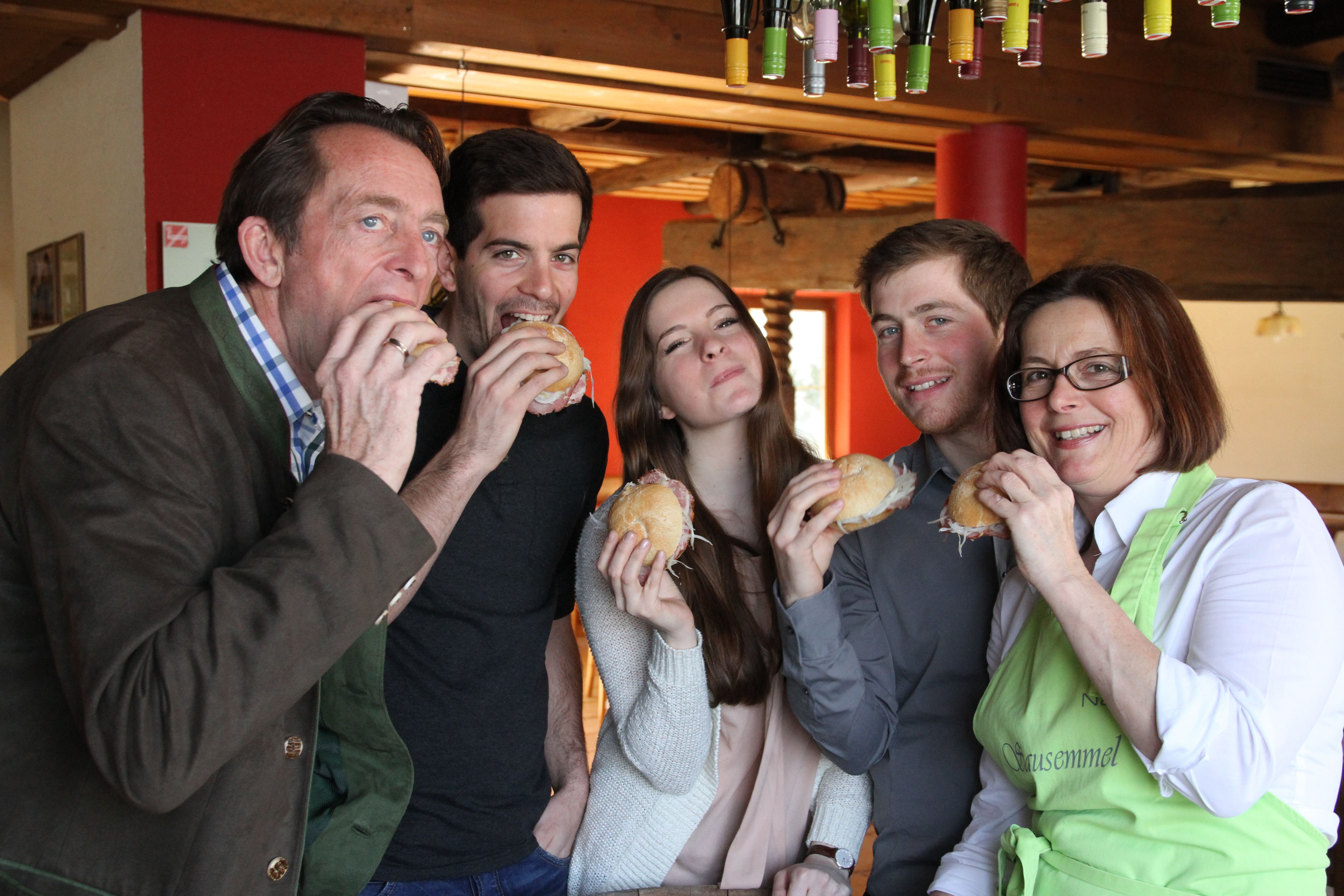 Fünf Personen essen gemeinsam belegte Brötchen in einem gemütlichen Raum.